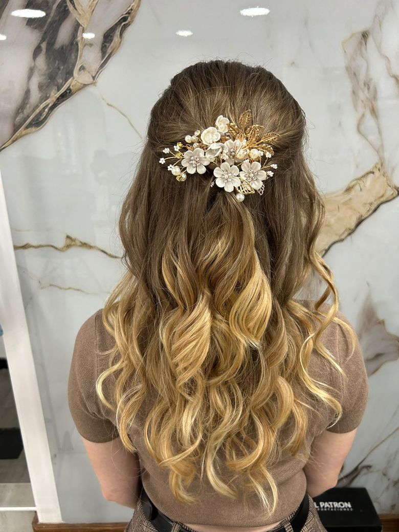 Semirrecogido con ondas y un tocado de flores blancas, perlas y hojas doradas, contra la pared de mármol