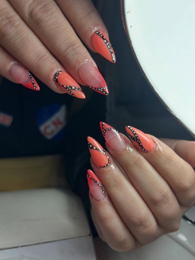Acrílicas stiletto con french naranja en diagonal, junto al aro de luz